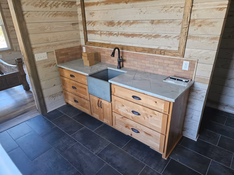 Rustic cabinetry with natural wood finish, stone countertop, and brick accent wall